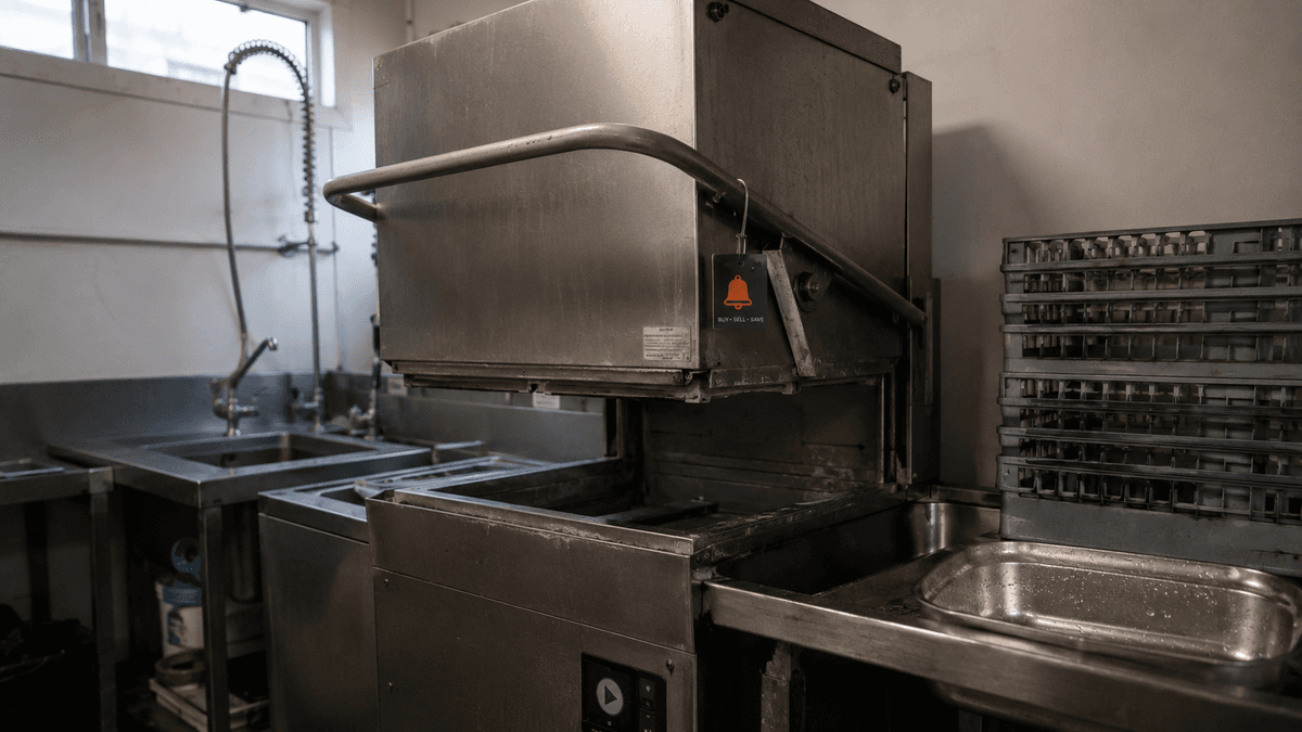 Used commercial pass-through dishwasher with its hood raised in a UK kitchen wash-up area, ready for inspection before sale.