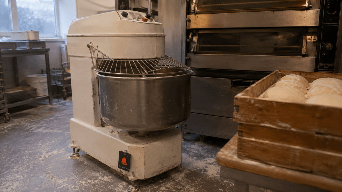 Used stainless spiral dough mixer and deck oven in a UK bakery unit, with a proving tray of dough nearby.