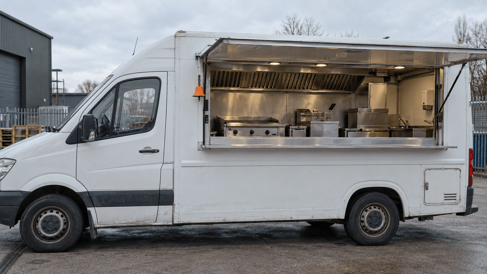 Used white catering van with the serving hatch open and a stainless steel kitchen inside, parked in a UK yard